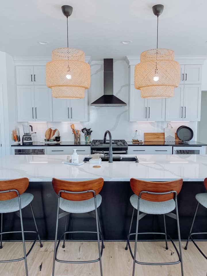 Modern kitchen with white cabinets, marble countertops, and black island with bar stools.