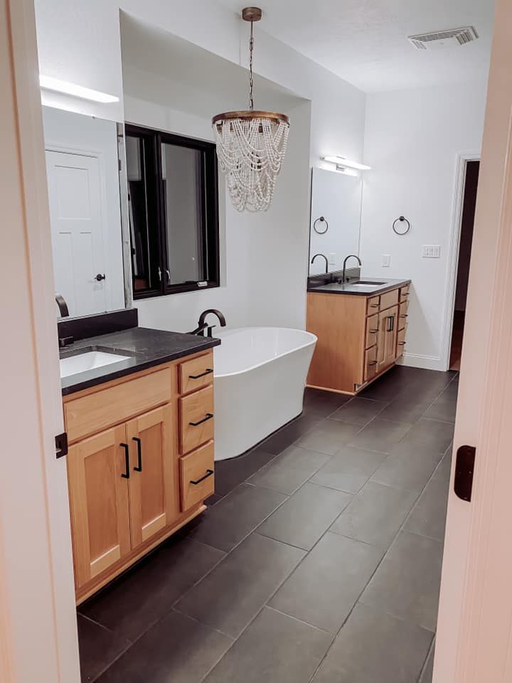 Spacious bathroom with wood vanities, dark floor, and a freestanding tub. 