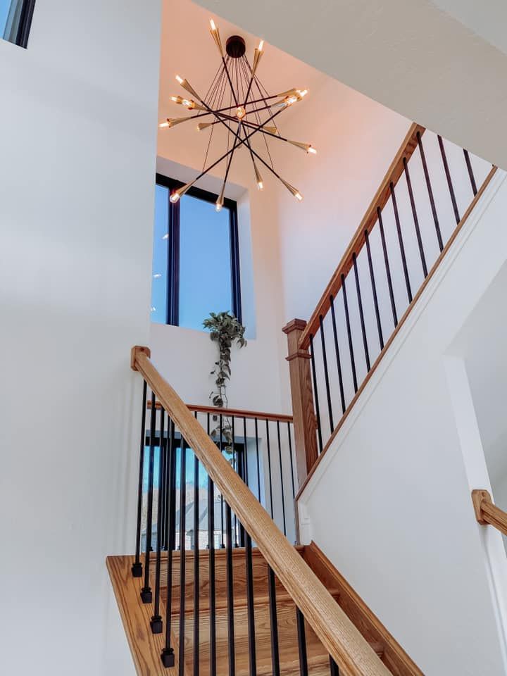 Wooden staircase with black railings, white walls, and a modern chandelier.