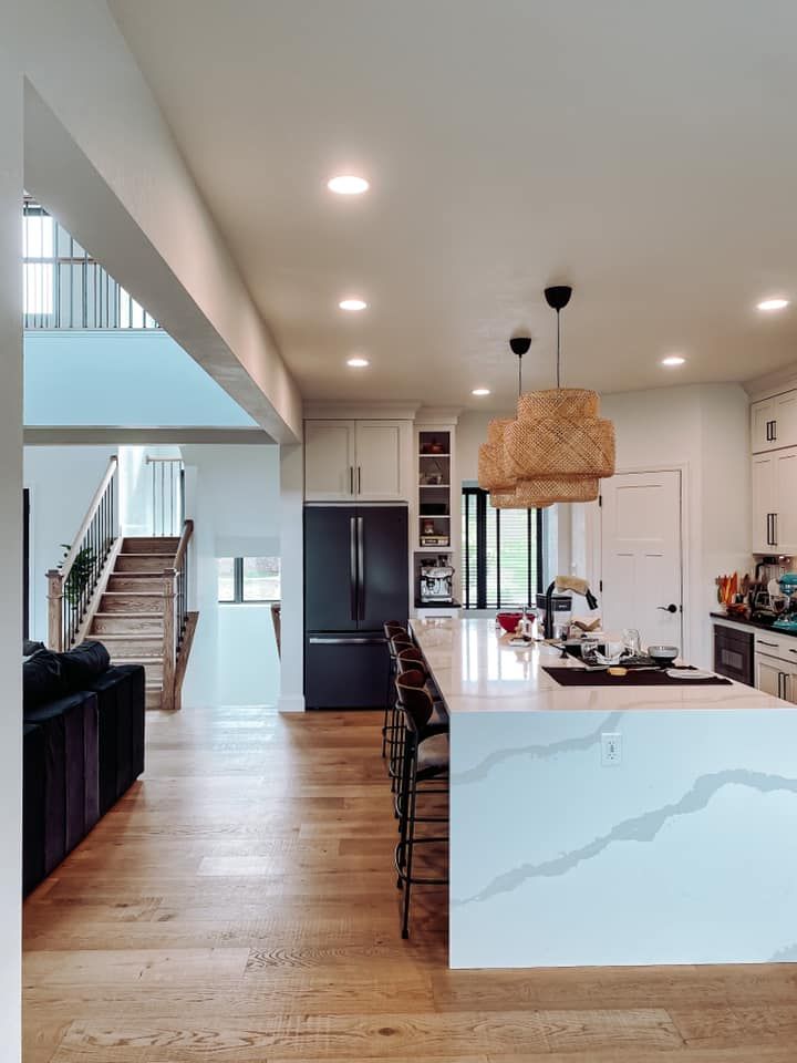 Modern kitchen with white cabinets, dark refrigerator, and large island with pendant lights.
