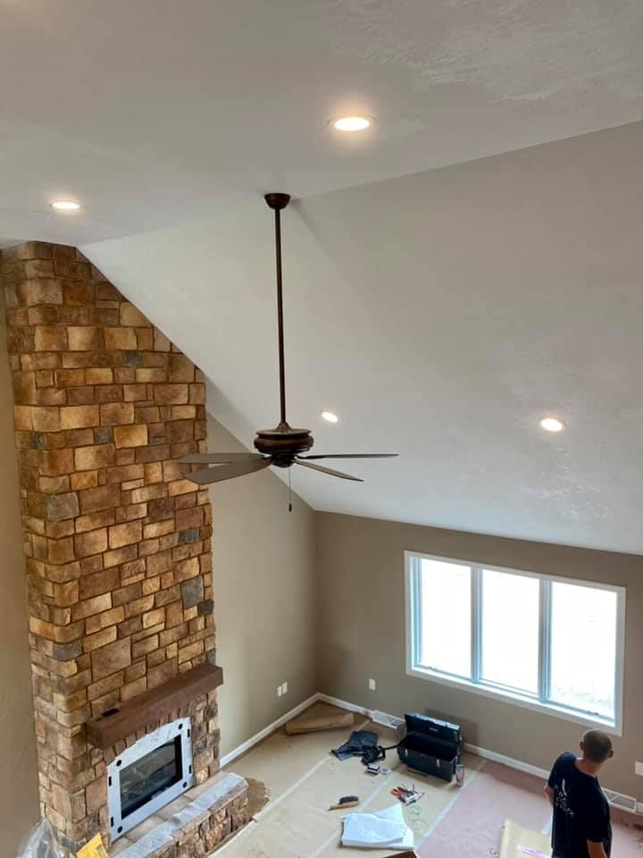 High-ceilinged living room with stone fireplace, ceiling fan, and recessed lighting.