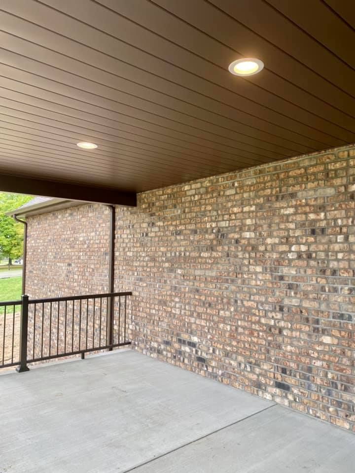 Brown brick exterior with concrete patio, dark ceiling, and two recessed lights.