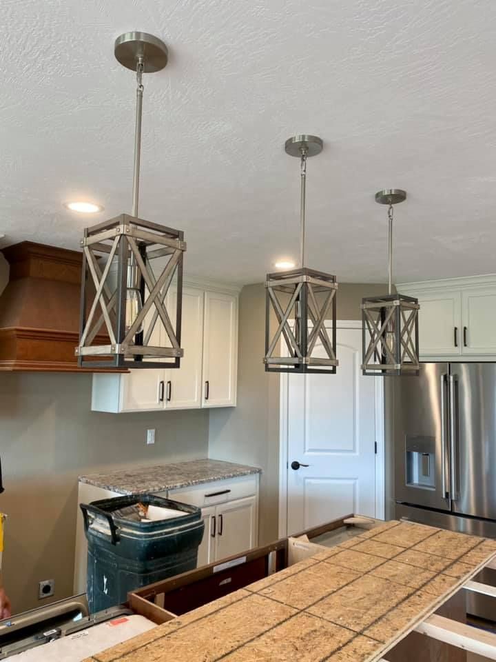 Three rustic pendant lights hang above a kitchen island with cabinets and appliances.