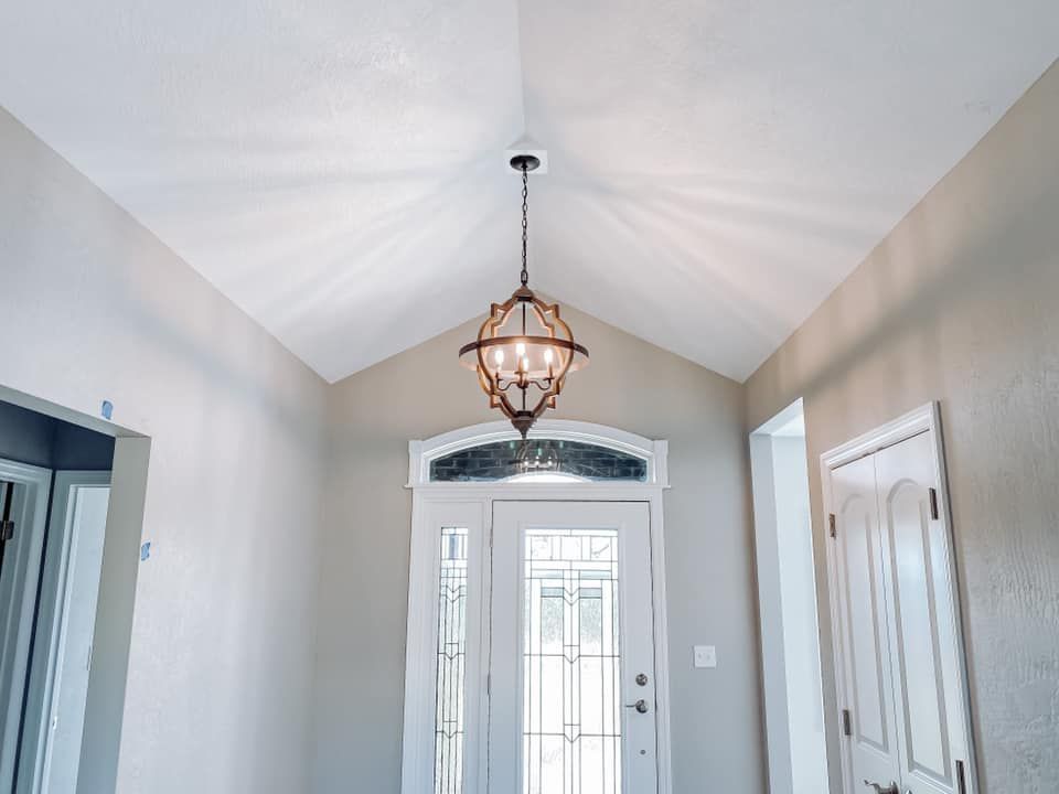 A light fixture hangs from a vaulted ceiling in a neutral-toned entryway. 