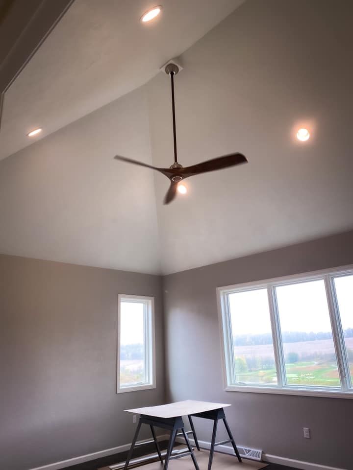 Room with vaulted ceiling, ceiling fan, recessed lights, windows, and a sawhorse table.