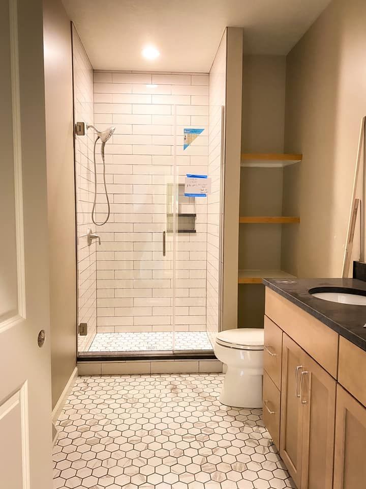 Modern bathroom with tiled shower, shelves, light wood vanity, and patterned floor.
