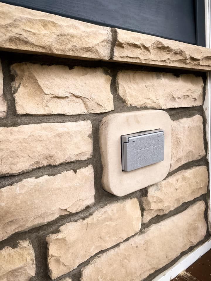 Exterior electrical outlet on stone wall, gray cover.
