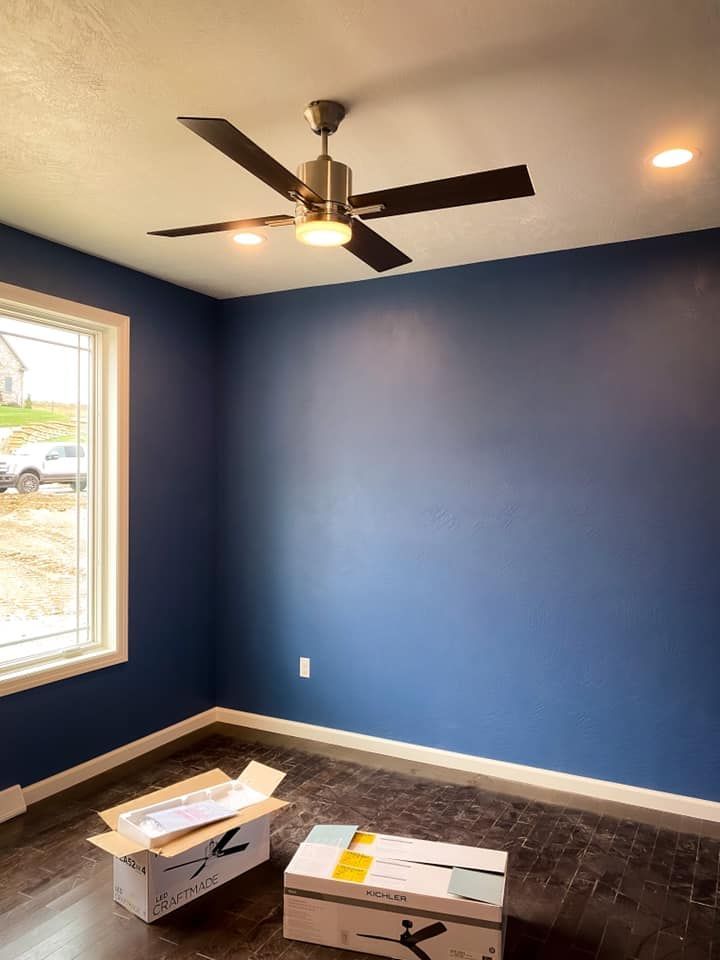 Blue-walled room with a ceiling fan, window, and boxes on the floor.