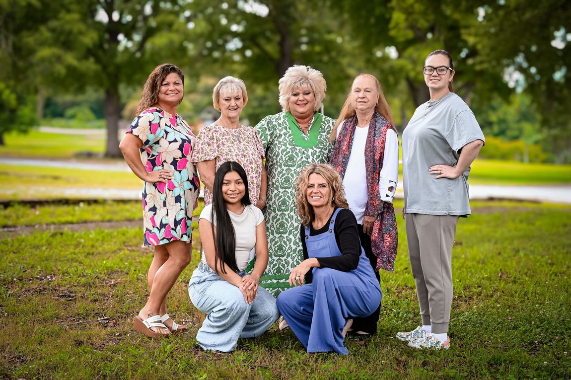 Six people posing together outdoors in a green park, smiling at the camera.