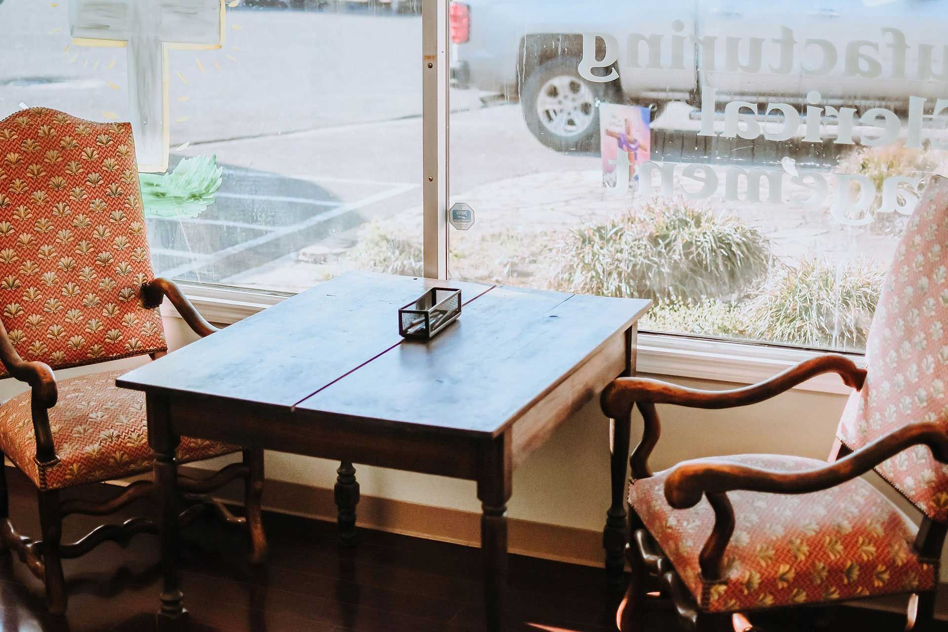 a wooden table and two ornate chairs sit by a window