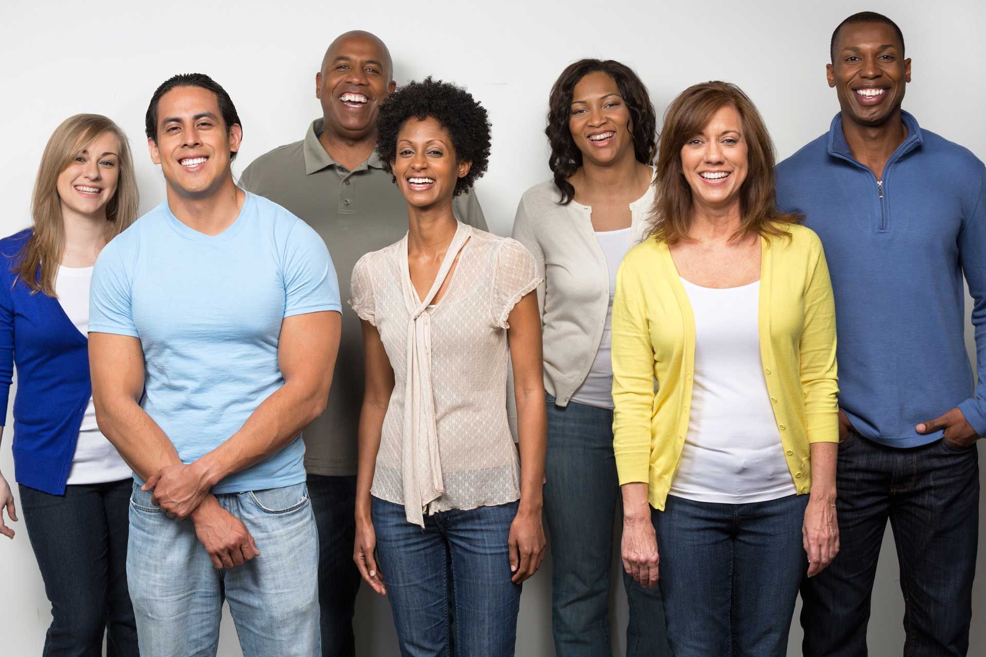 a group of diverse people smiling, standing in front of a white wall