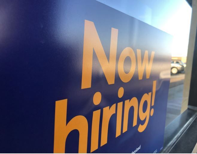 A blue and orange sign that says now hiring.