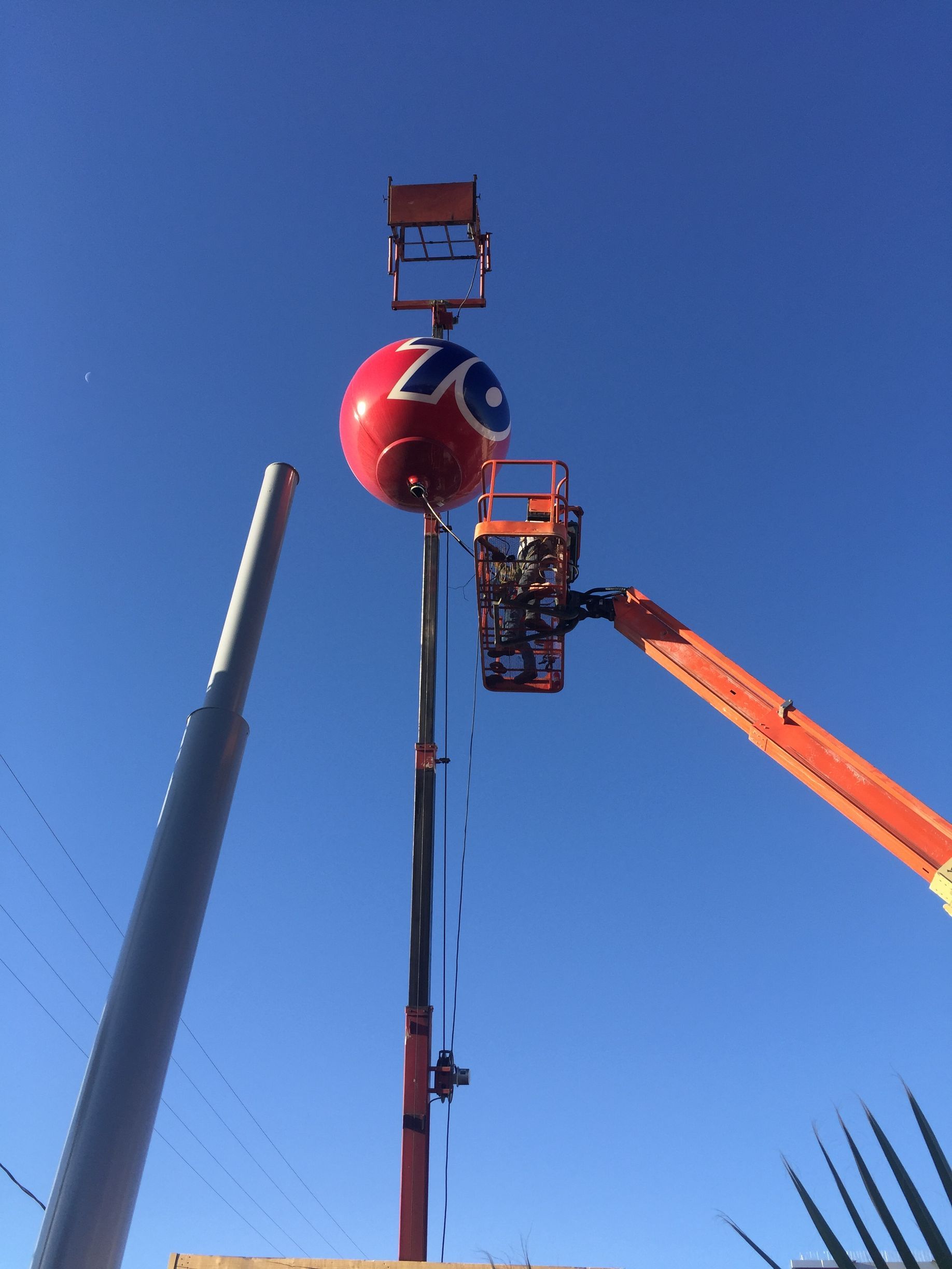 A crane is lifting a large red ball signage.