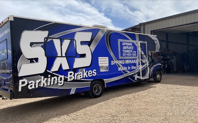 A blue truck with the words sxs parking brakes on the side is parked in front of a building.