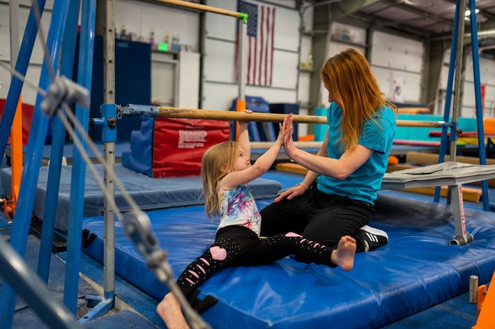 A woman and a little girl are sitting on a mat in a gym.