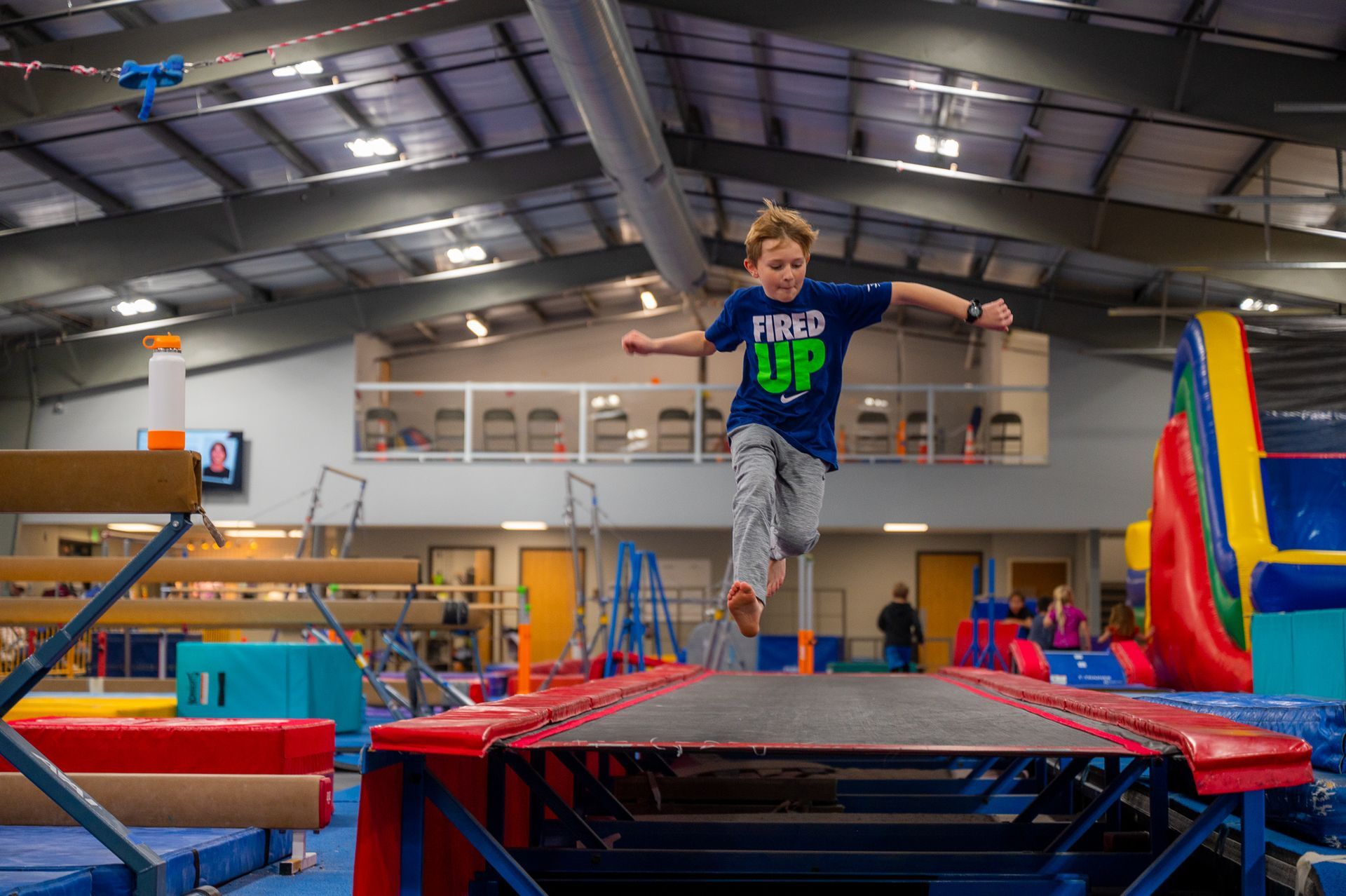A young boy is jumping on a trampoline in a gym.