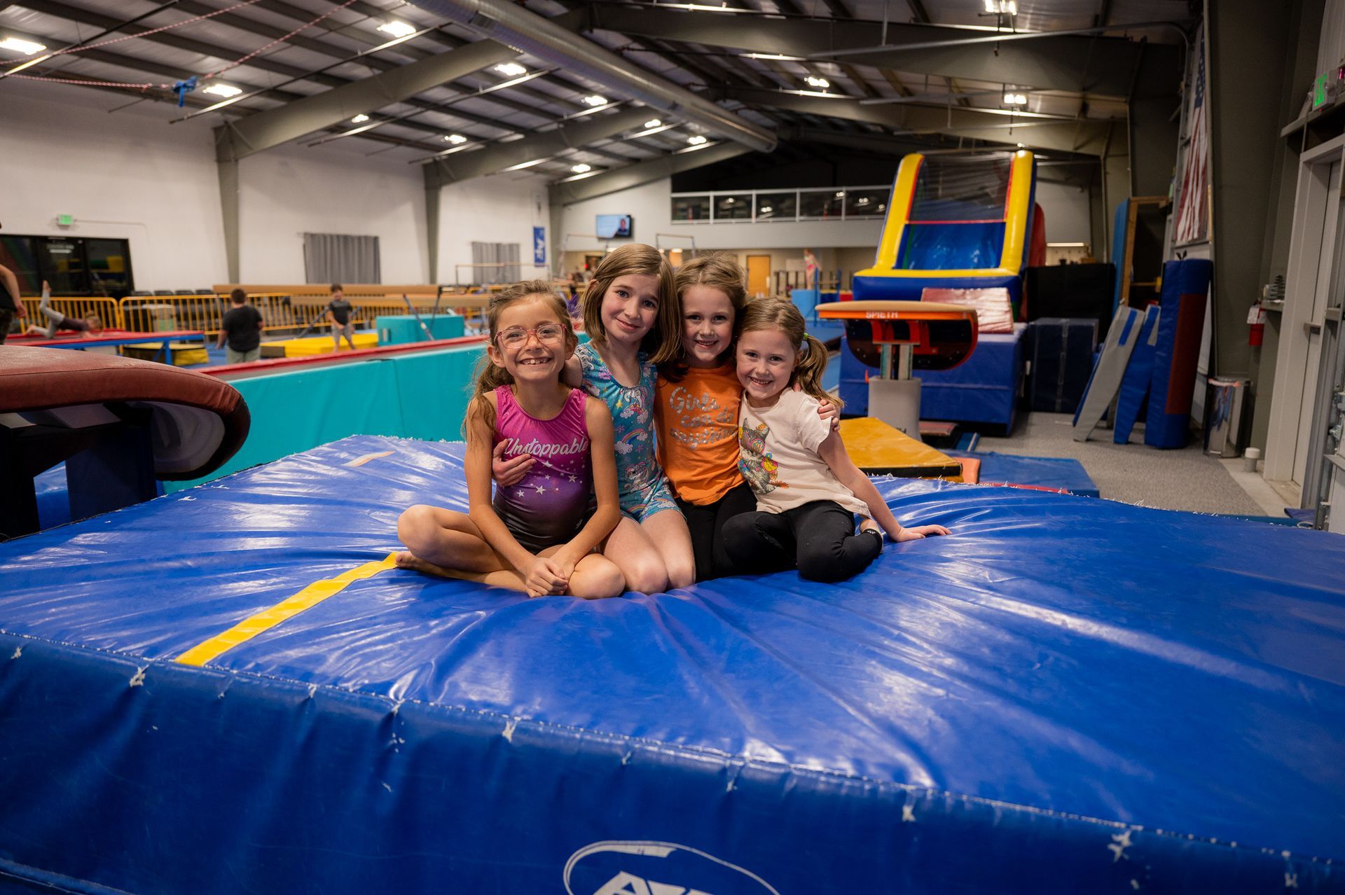 A group of young girls are sitting on a blue mat in a gym.
