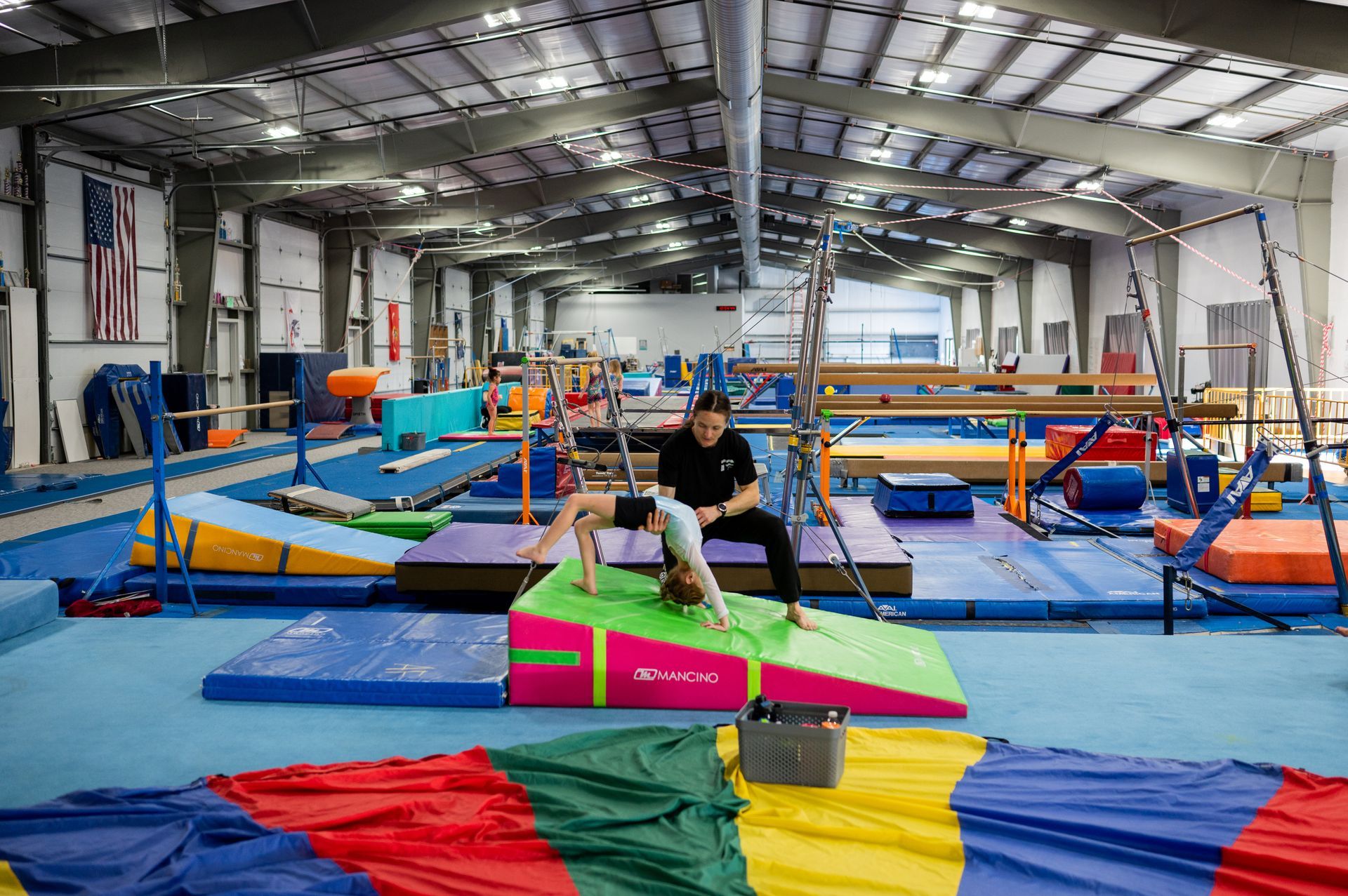 A man is sitting on a mat with a child in a gym.