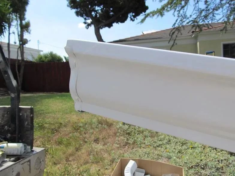 A white gutter is sitting in the grass next to a cardboard box