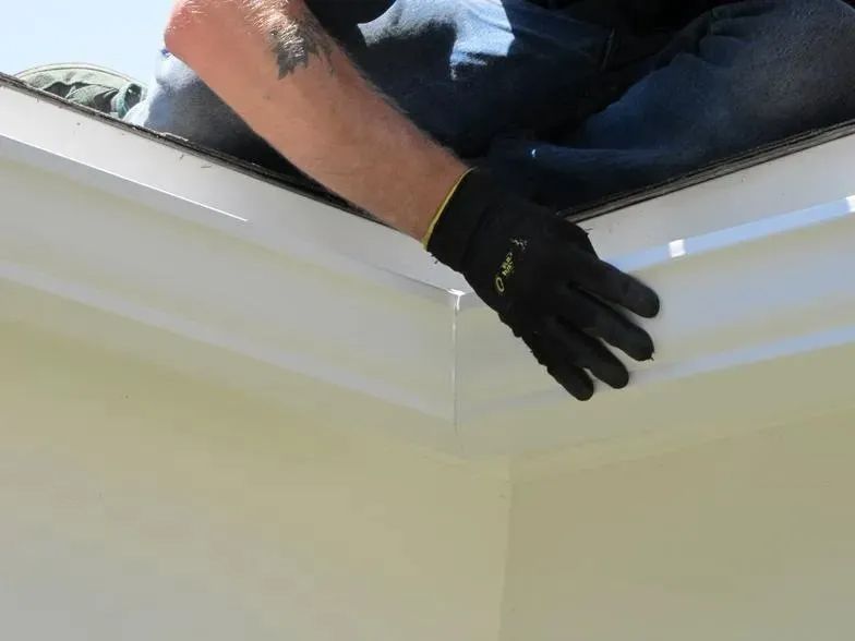 A man wearing gloves is working on the roof of a house.