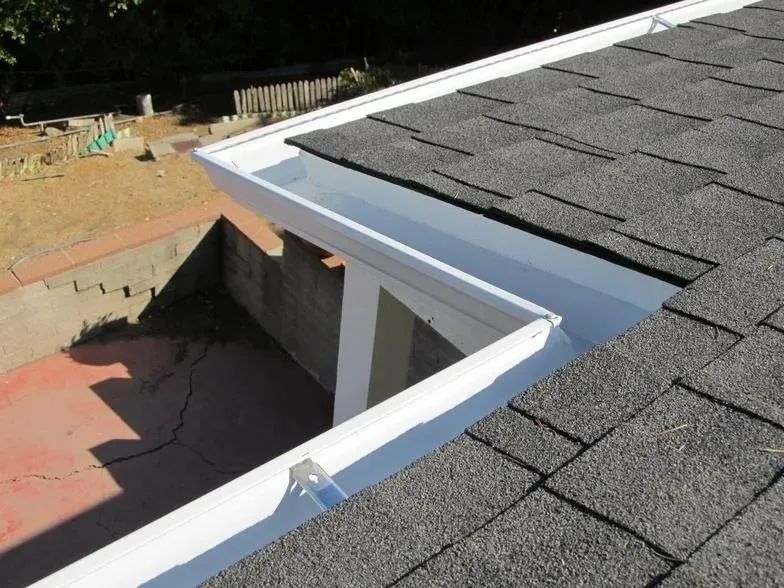 A white gutter on a roof with shingles