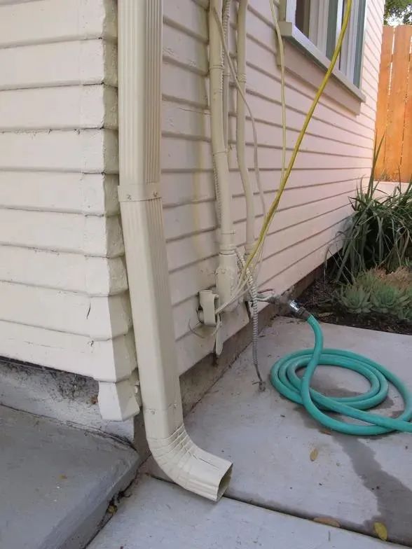 A green hose is attached to the side of a house