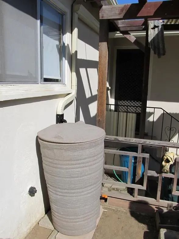 A gray water barrel is sitting outside of a house