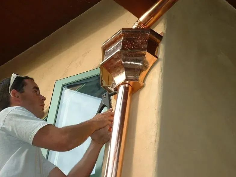 A man is working on a copper pipe on the side of a building
