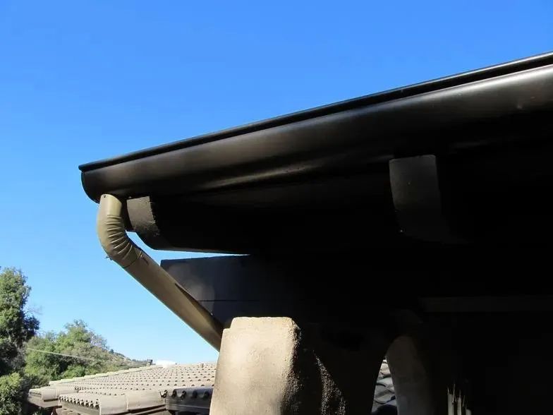 A close up of a gutter on a roof with a blue sky in the background