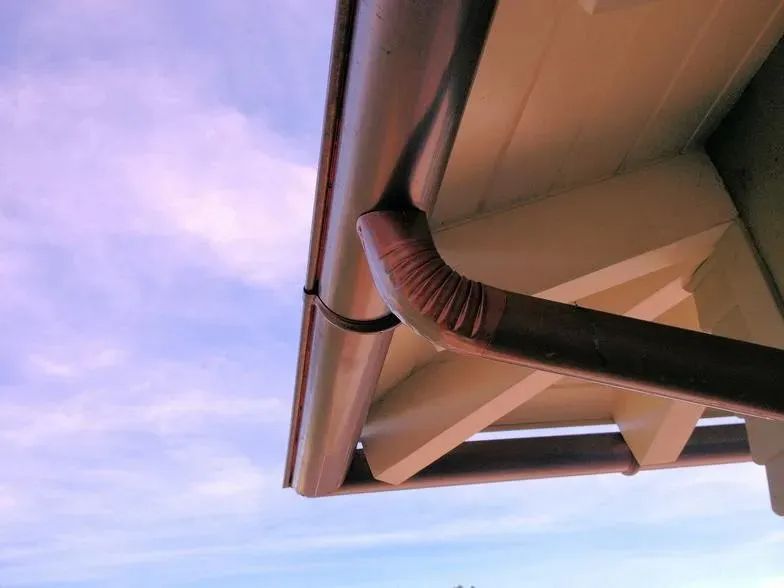 A close up of a gutter on a roof with a blue sky in the background.