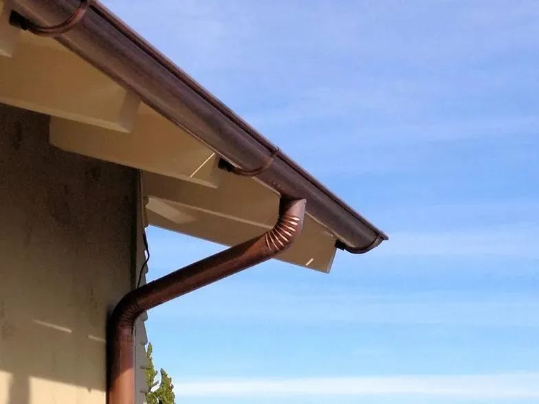 A brown gutter on the side of a house with a blue sky in the background