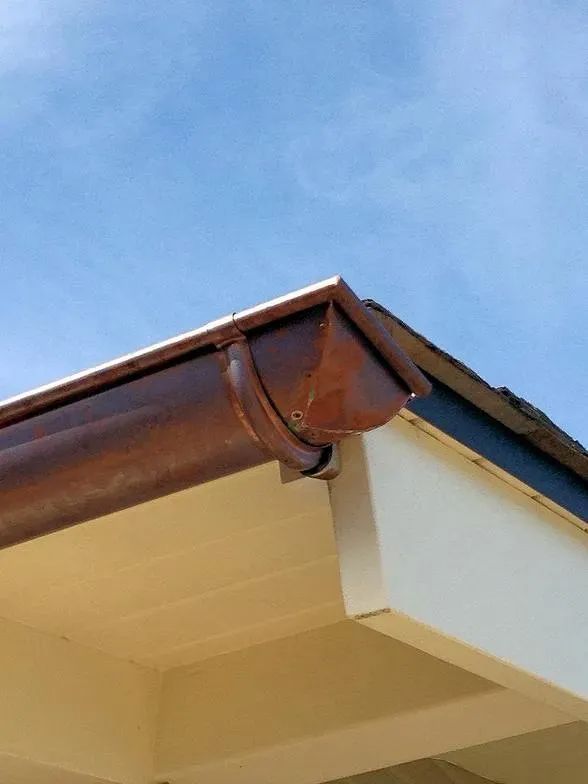 A close up of a gutter on a roof with a blue sky in the background.