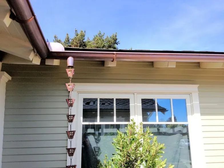 A rain chain is hanging from the gutter of a house.