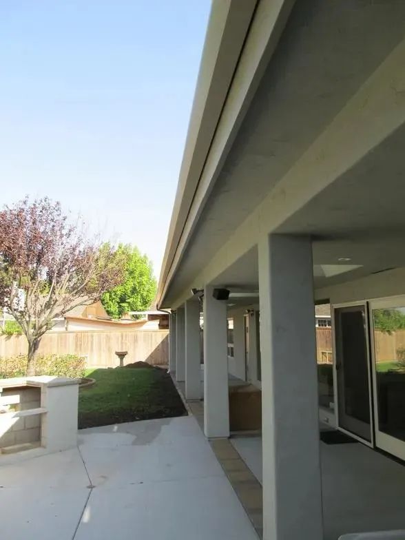 A covered patio with columns and a fence in the background