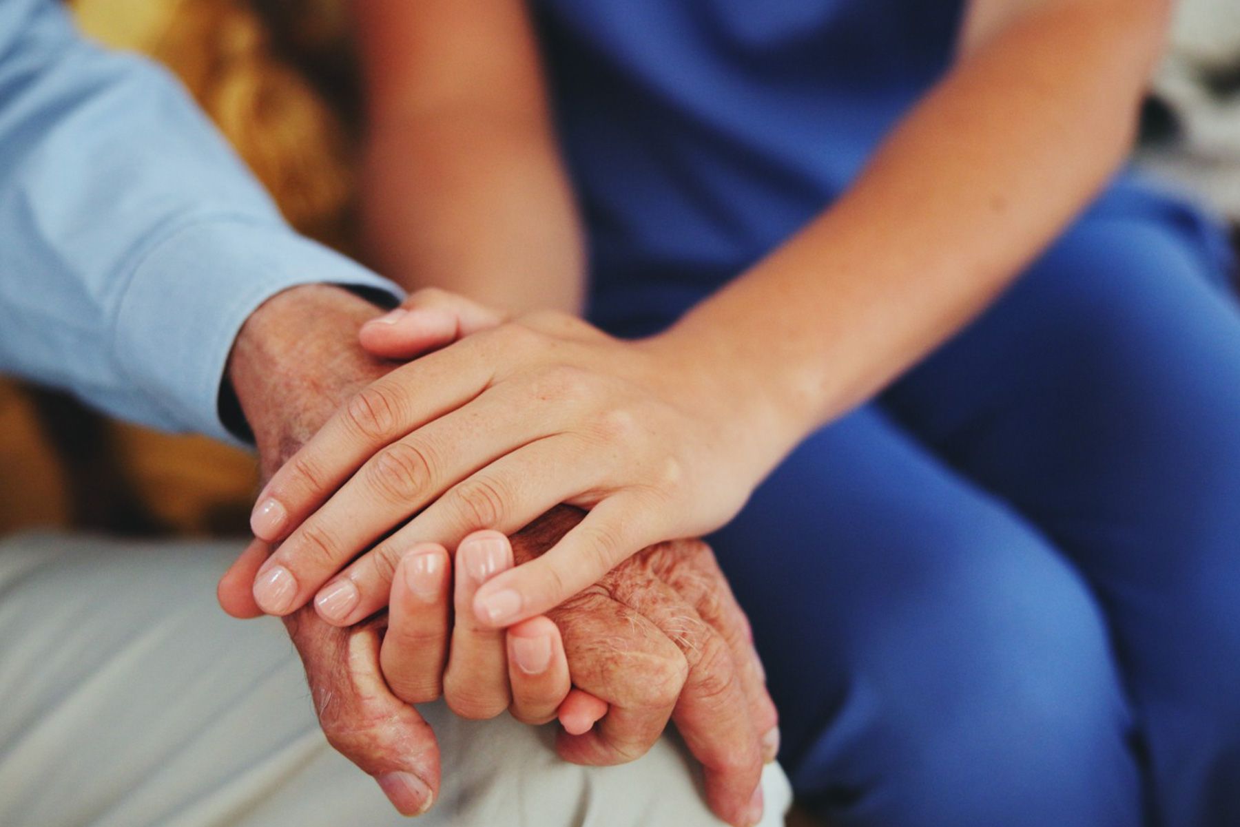 A nurse is holding the hands of an older man.