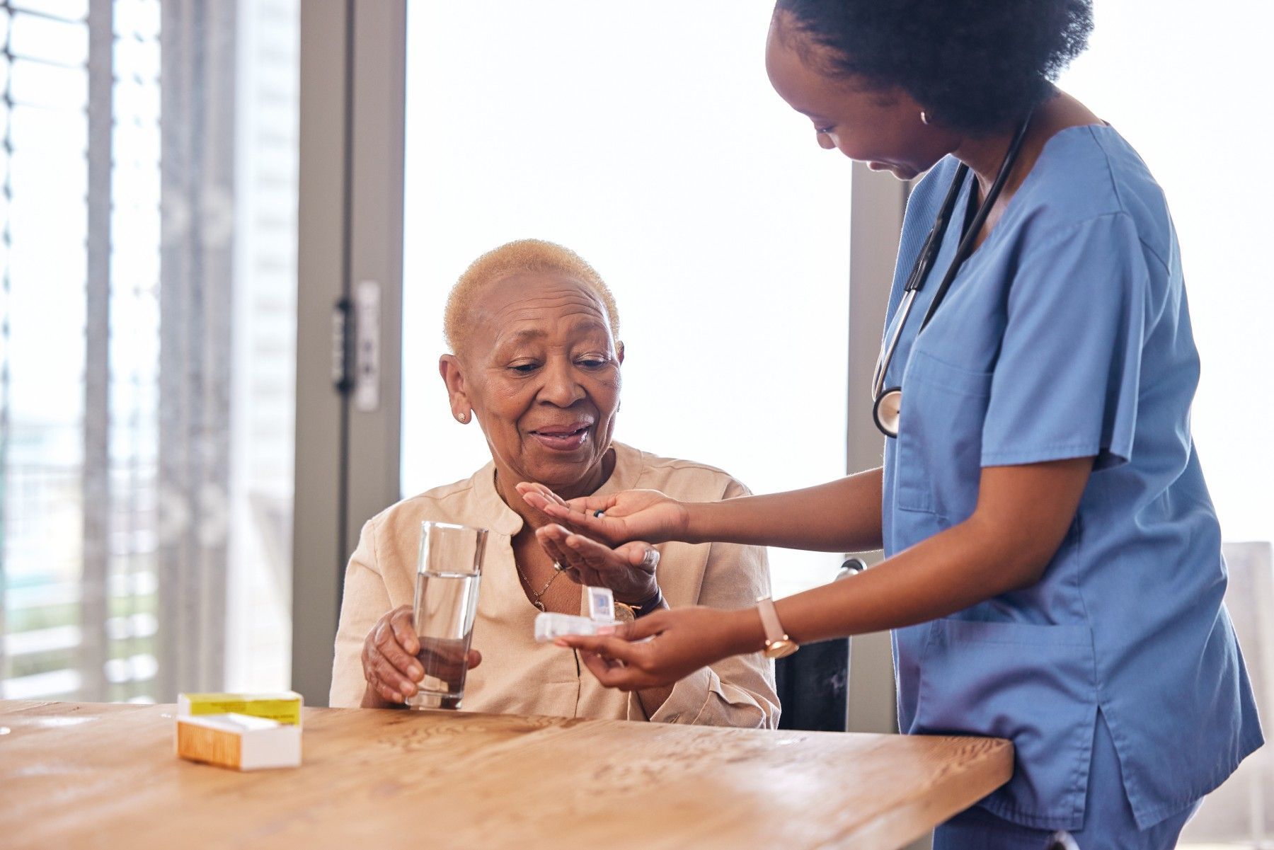 A nurse is giving an elderly woman a glass of water and pills.