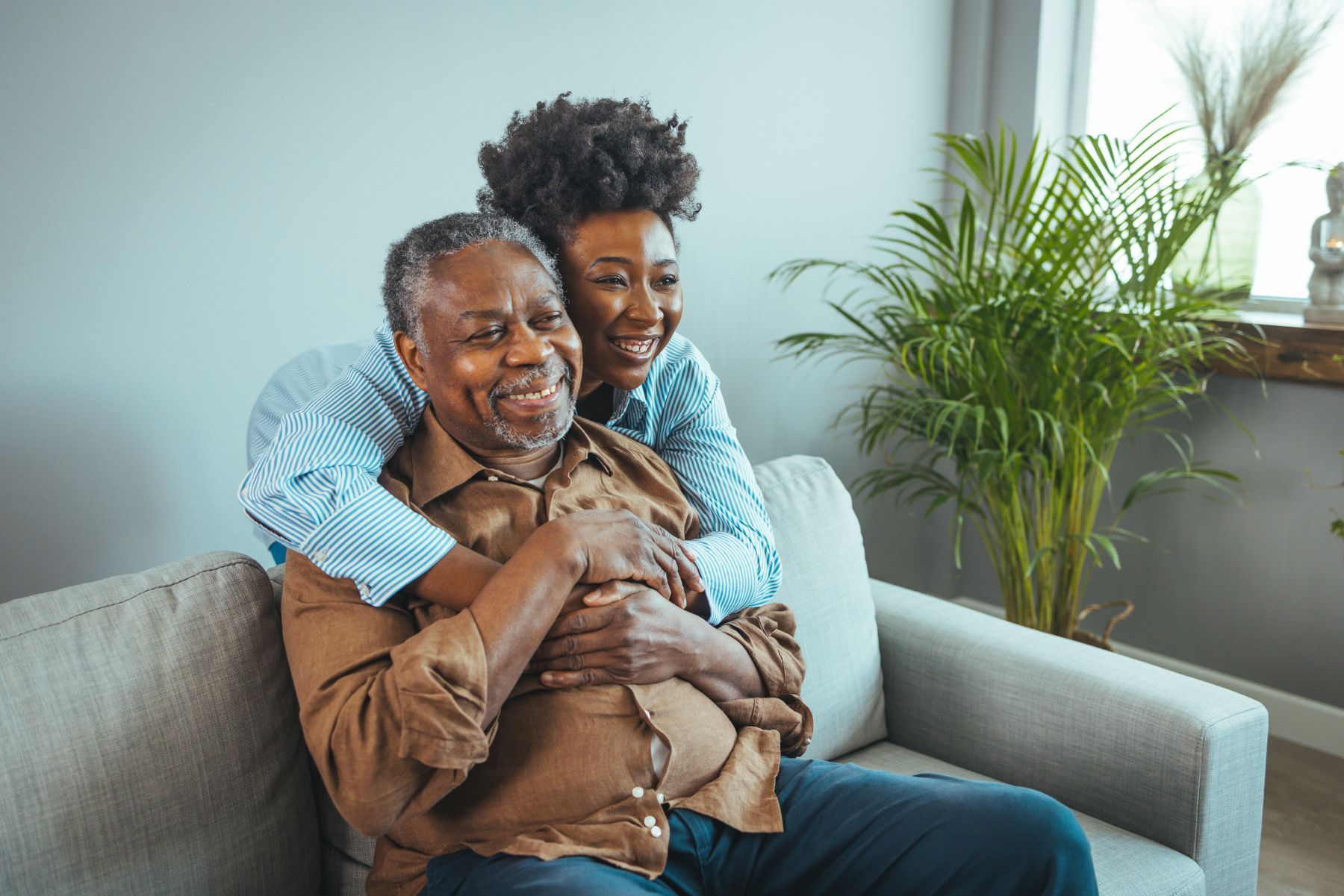 A woman is hugging an older man on a couch.