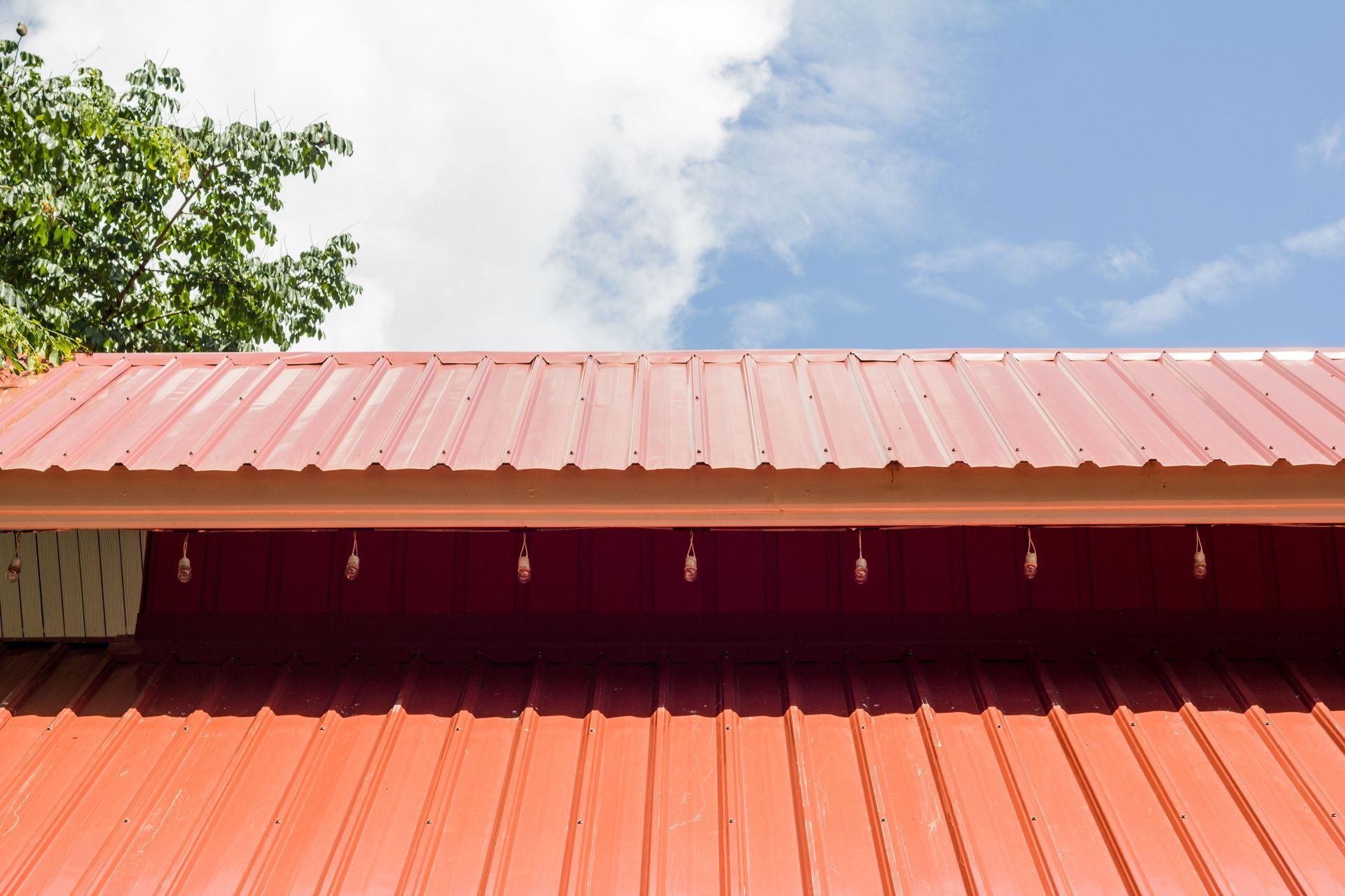 Red metal roof against a partly cloudy sky, with a tree in the background.