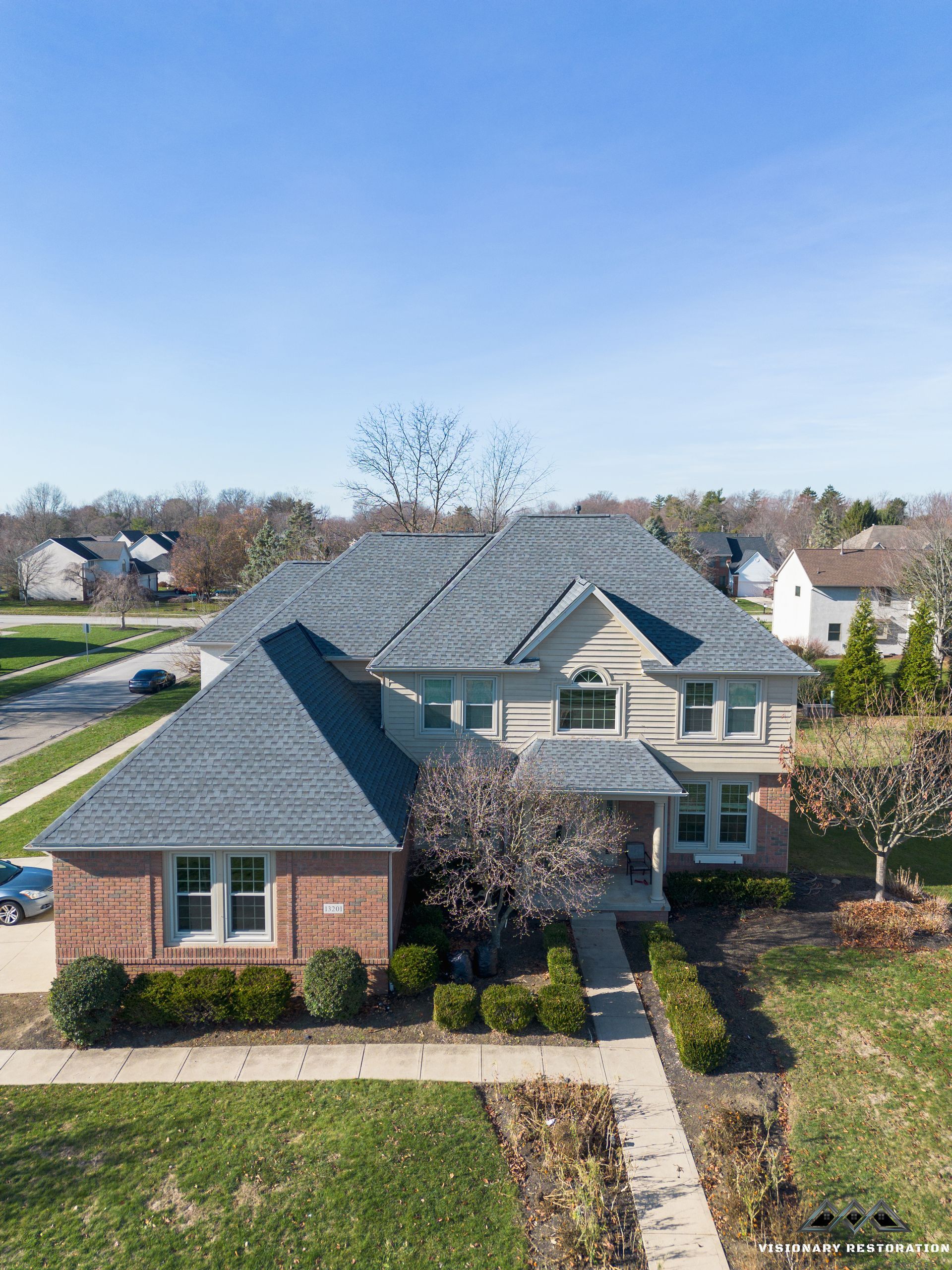 Two-story brick house with a dark gray roof on a sunny day.