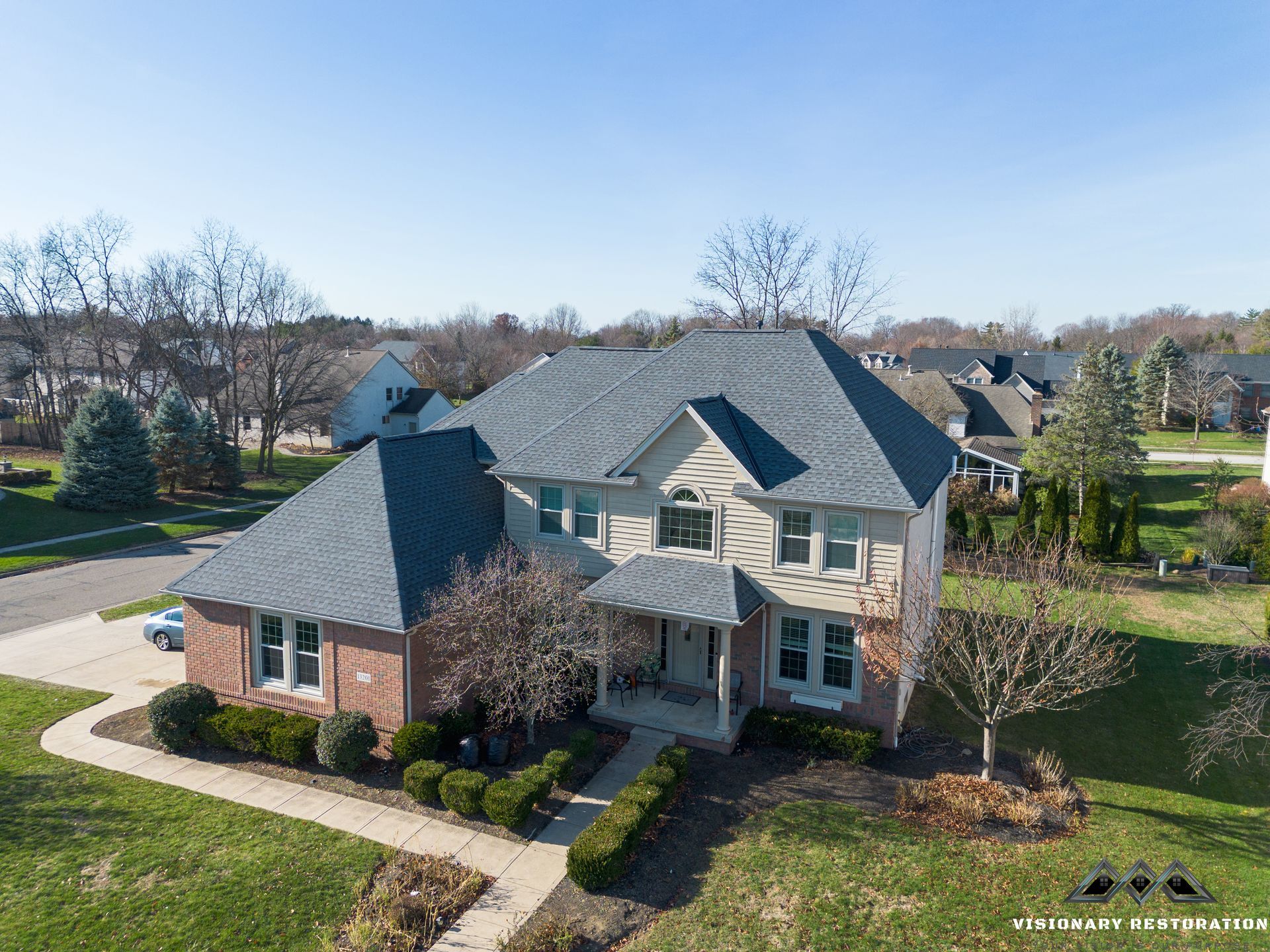 Aerial view of a two-story house with a gray roof and brick facade on a sunny day.