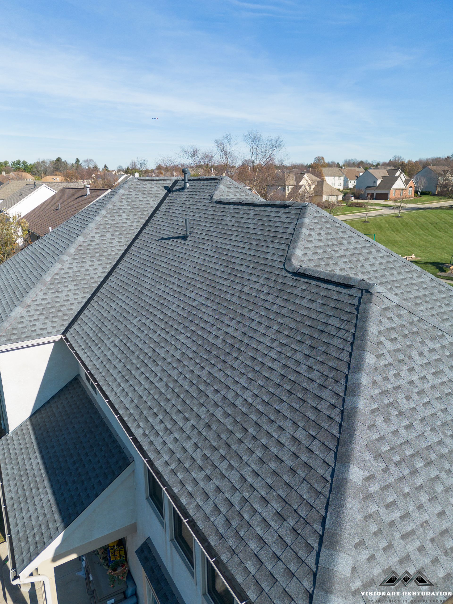 Overhead view of a house roof with dark gray shingles, under a blue sky.