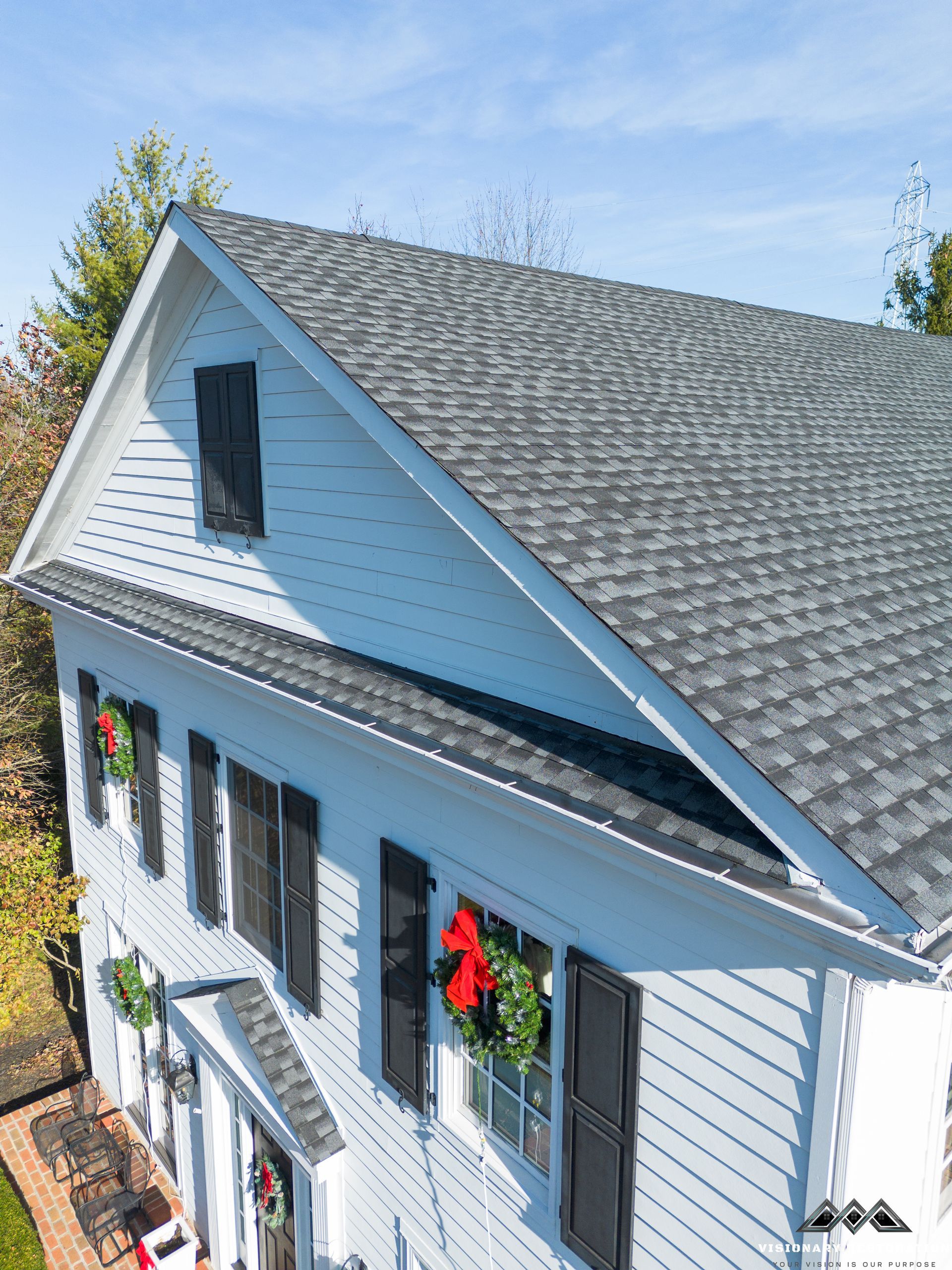 White house with gray shingle roof and black shutters, decorated with red bows.