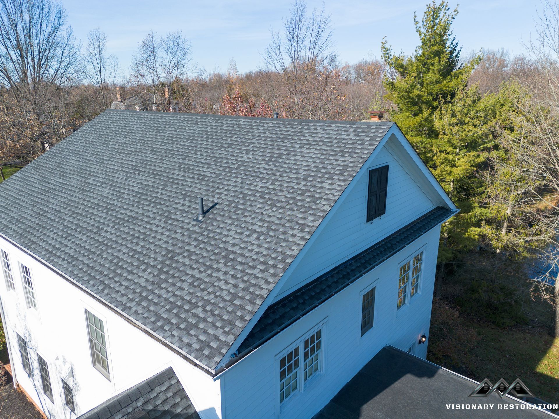 White house with a dark gray shingled roof, trees in the background, blue sky.