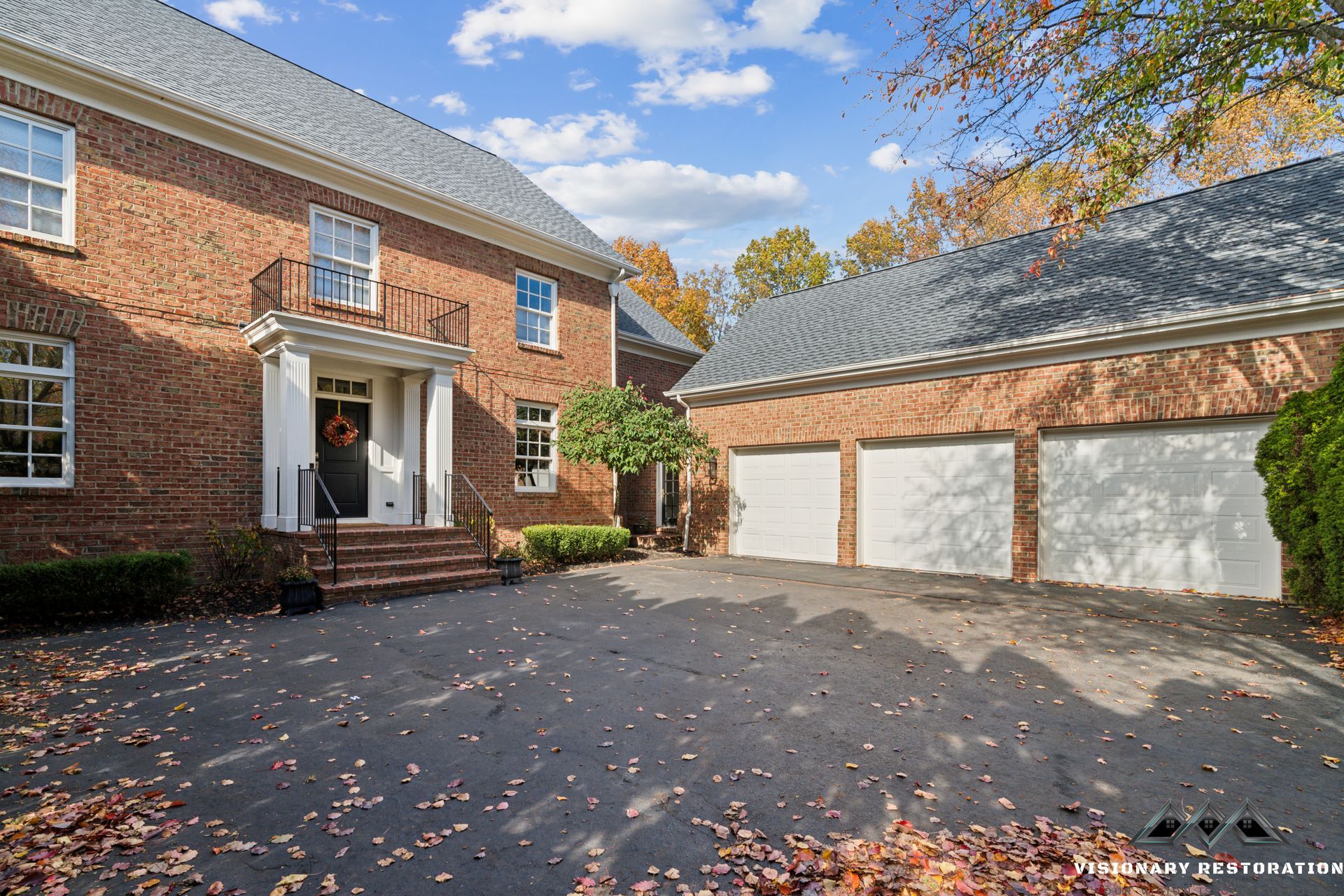Brick house with a three-car garage and a driveway covered in fall leaves.