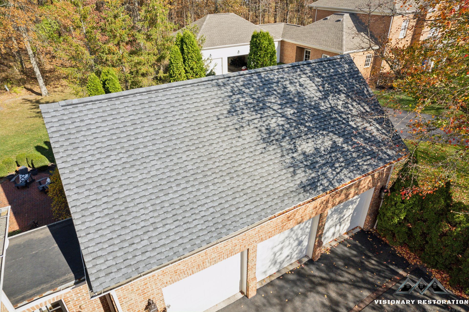 A gray-shingled roof on a brick garage with three white garage doors, viewed from above.