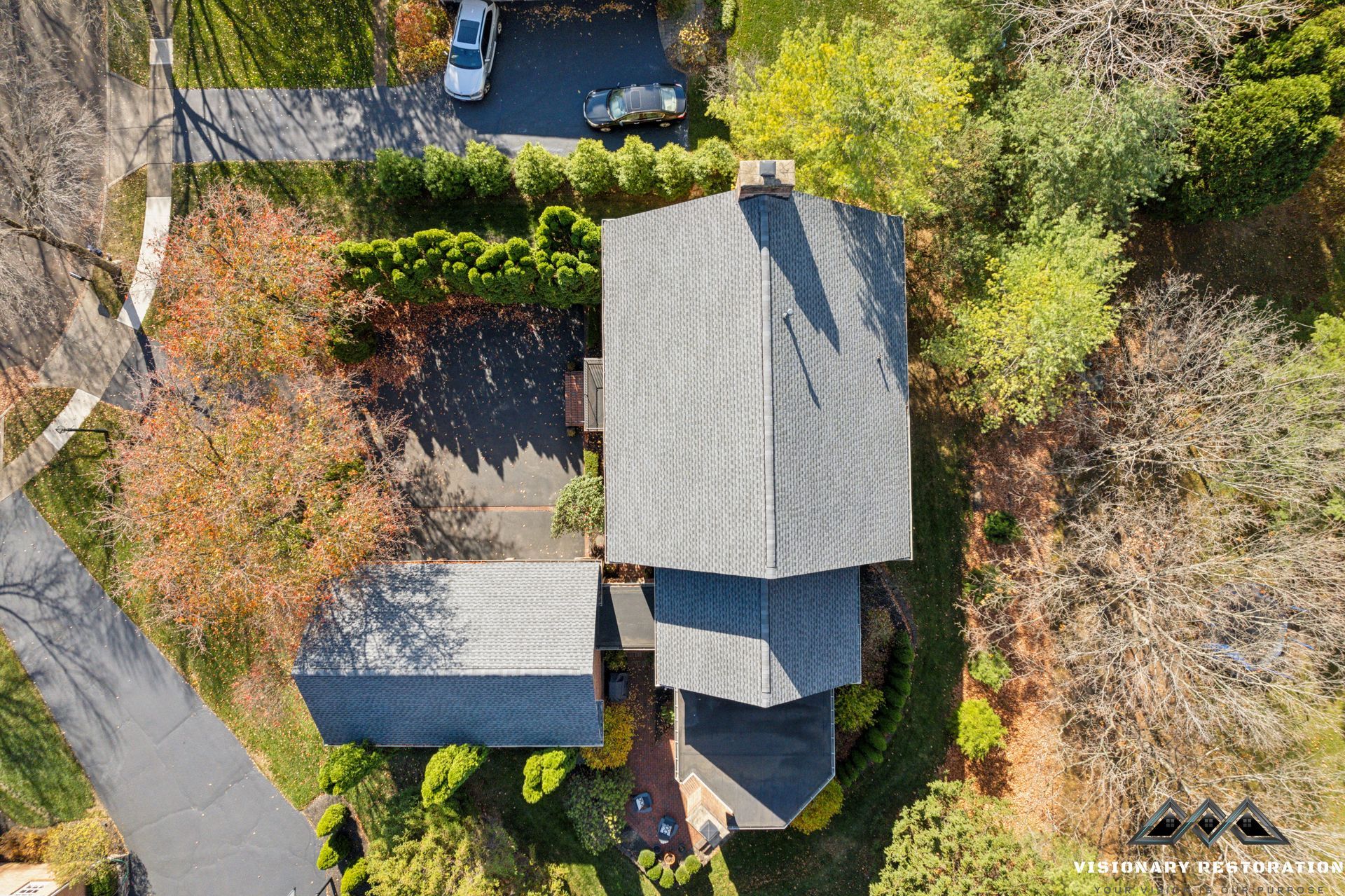 Overhead view of a house with a gray roof and driveway, surrounded by trees and green foliage.