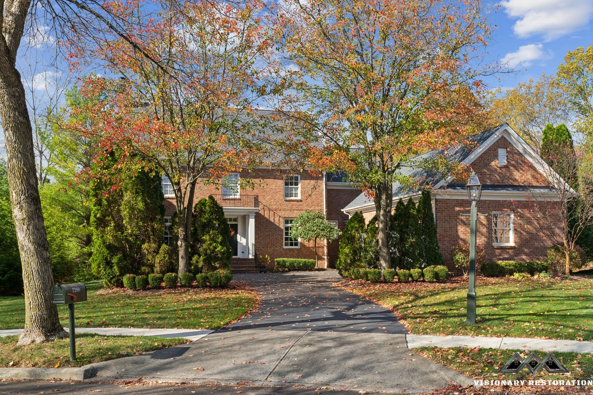 Brick house with curved driveway and autumn trees.