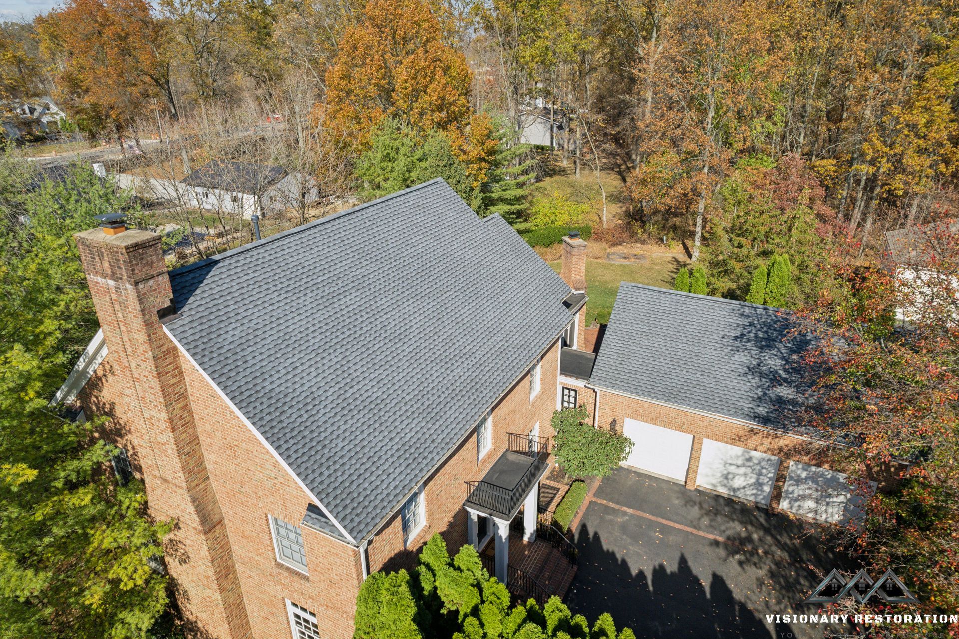 Aerial view of a brick house with a dark gray roof surrounded by trees in autumn.