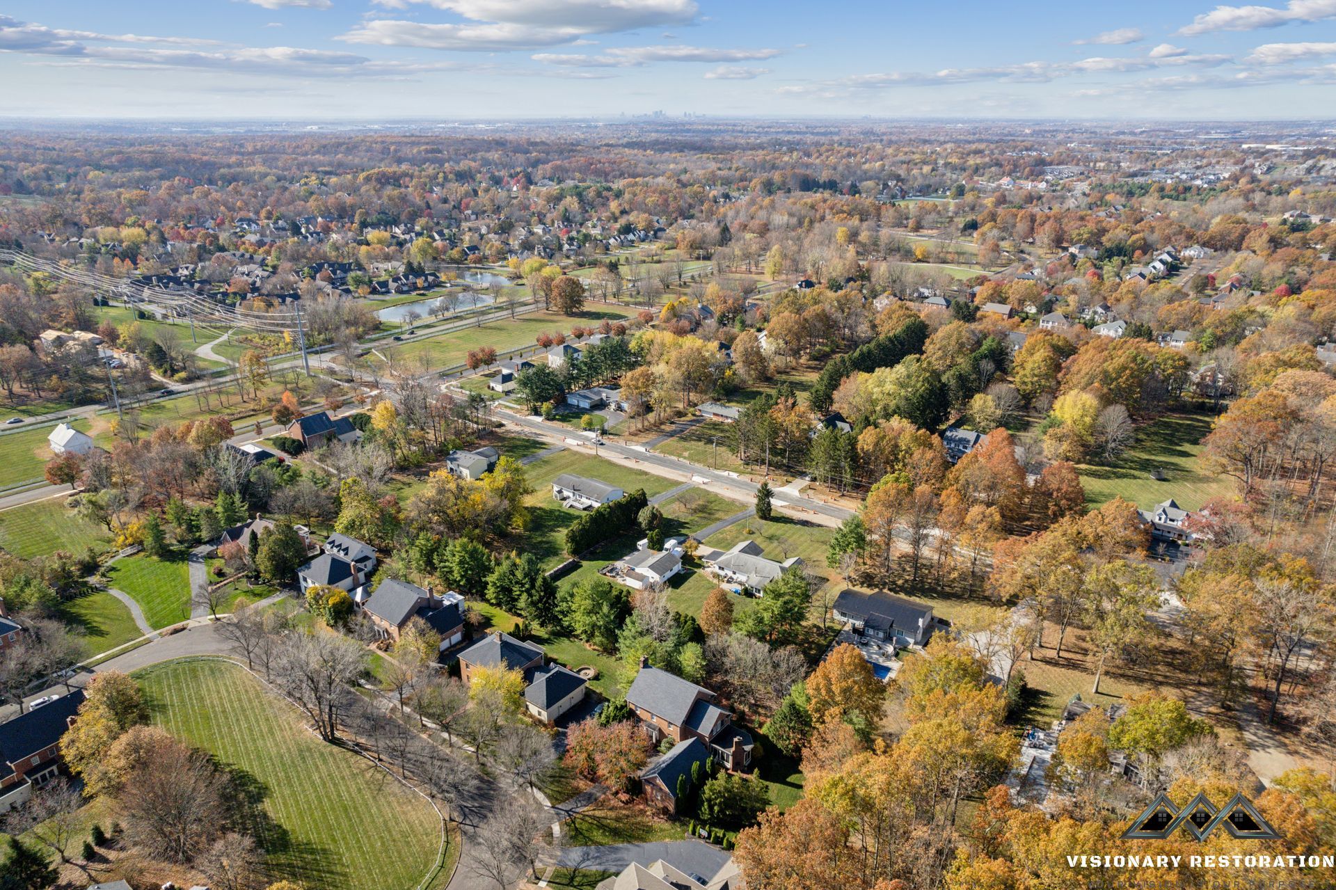 Aerial view of a suburban neighborhood in autumn; trees with colorful foliage surround houses and roads.