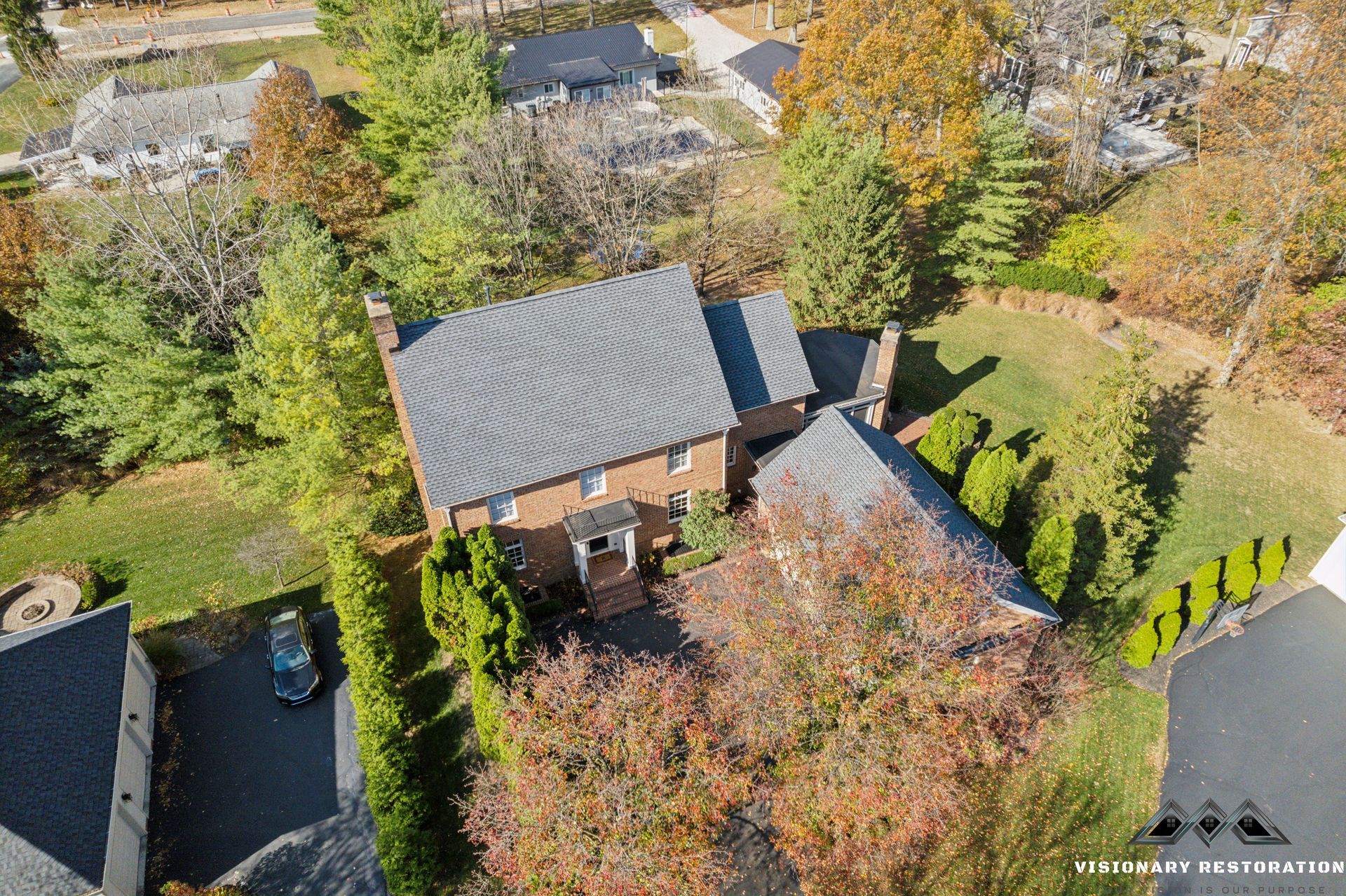 Aerial view of a two-story brick house with a gray tile roof, surrounded by trees and a driveway.